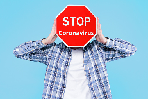 Young man is holding warning red sign symbol stop coronavirus. Virus SARS-CoV-2, 2019-nCoV that leads to infectious respiratory illness disease Covid-19, pneumonia. Pandemic epidemic concept.