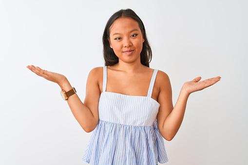 Young chinese woman wearing casual striped dress standing over isolated white background clueless and confused expression with arms and hands raised. Doubt concept.