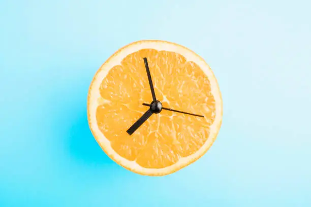 Photo of Fresh orange with clock arrows. Healthy nutrition/healthy lifestyle concept on blue background.