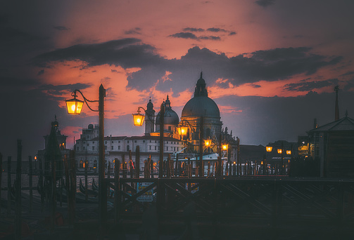 Scenic view of Santa Maria della Salute Basilica and illuminated street lamps standing near the grand canal with dramatic cloudy sunset sky in Old town of  Venice, Italia