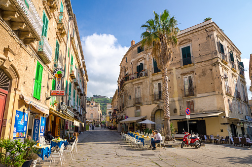 Tropea, Italy - May 9, 2018: Streets of town with cafes and restaurants, motorcycle bike Vespa, buildings with balconies and shutter windows, blue sky with clouds on backgrond, Calabria