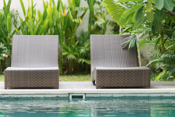Swimming pool with rattan chair outdoors at sunny day Swimming pool with brown rattan chair on poolside against natural green background standing on private territory at summer sunny day chaise longue stock pictures, royalty-free photos & images