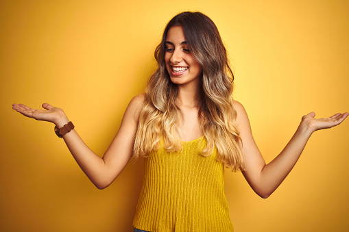 Young beautiful woman wearing t-shirt over yellow isolated background smiling showing both hands open palms, presenting and advertising comparison and balance