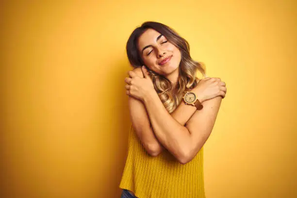 Young beautiful woman wearing t-shirt over yellow isolated background Hugging oneself happy and positive, smiling confident. Self love and self care