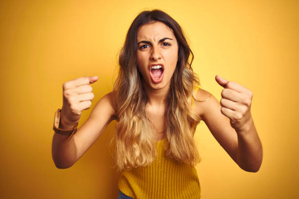 Young beautiful woman wearing t-shirt over yellow isolated background angry and mad raising fists frustrated and furious while shouting with anger. Rage and aggressive concept. Young beautiful woman wearing t-shirt over yellow isolated background angry and mad raising fists frustrated and furious while shouting with anger. Rage and aggressive concept. fist human hand punching power stock pictures, royalty-free photos & images