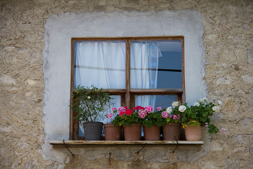 A wooden framed window of a traditional alpine hut with red and yellow flowers. Square format.