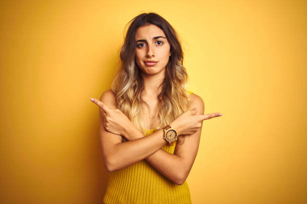 黄色の孤立した背景の上にtシャツを着た若い美しい女性は指で両側を指差し、異なる方向は反対する - space to left ストックフォトと画像