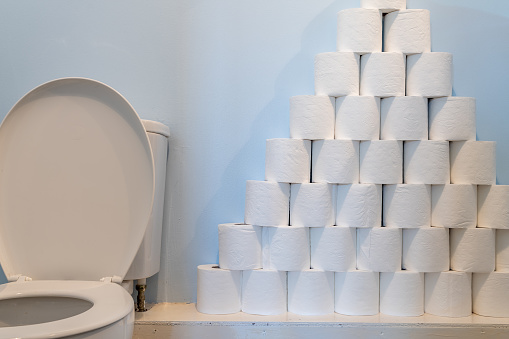 A huge pile of toilet paper stacked up next to a toilet