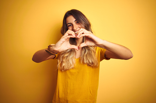 Young beautiful woman wearing t-shirt over yellow isolated background smiling in love showing heart symbol and shape with hands. Romantic concept.