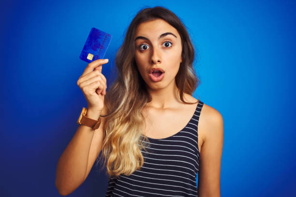 파란 고립 된 배경위에 신용 카드를 들고있는 젊은 아름다운 여성은 깜짝 얼굴로 충격에 무서워하고 두려움과 두려움표현으로 흥분했습니다. - mouth open retail shock surprise 뉴스 사진 이미지