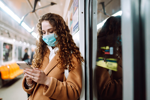 Girl in protective sterile medical mask on her face with a phone in a subway car. Woman using the phone to search for news about coronavirus. The concept of preventing the spread of the epidemic.