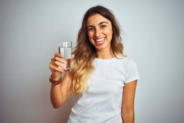 junge schöne frau trinkt ein glas wasser über weißen isolierten hintergrund mit einem glücklichen gesicht stehen datund lächelnd mit einem selbstbewussten lächeln zeigt zähne - toothy smile relaxation white healthcare and medicine stock-fotos und bilder