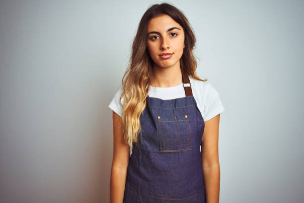 istock Young beautiful woman wearing apron over grey isolated background with serious expression on face. Simple and natural looking at the camera. 1214048644