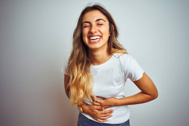 jovem linda mulher vestindo t-shirt branca casual sobre fundo isolado sorrindo e rindo muito alto porque piada louca engraçada com as mãos no corpo. - hard body - fotografias e filmes do acervo