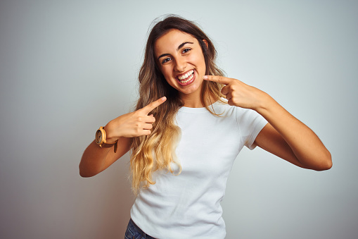 Young beautiful woman wearing casual white t-shirt over isolated background smiling cheerful showing and pointing with fingers teeth and mouth. Dental health concept.
