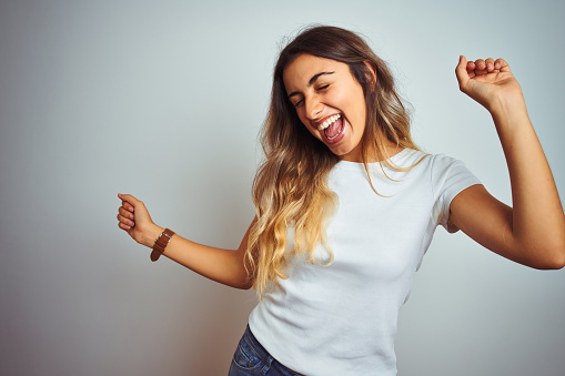 Young beautiful woman wearing casual white t-shirt over isolated background Dancing happy and cheerful, smiling moving casual and confident listening to music