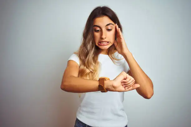 Photo of Young beautiful woman wearing casual white t-shirt over isolated background Looking at the watch time worried, afraid of getting late