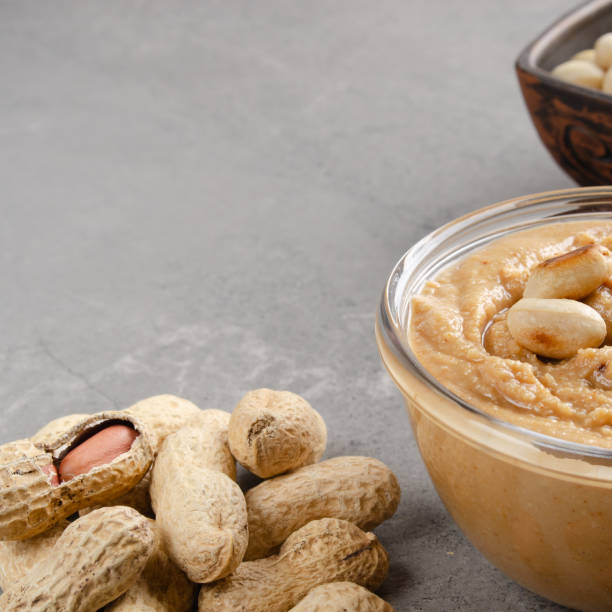 istock Low angle view at glass bowl with peanut butter on stone table. Healthy eating concept 1214052714