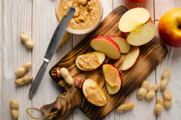 Flat lay view at Cut board with apple slices with peanut butter on white wooden kitchen table