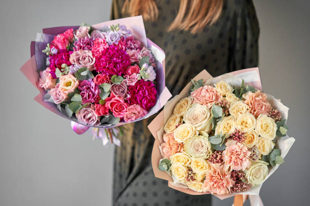 due bellissimi mazzi di fiori misti in mani di donna. lavoro del fioraio in un negozio di fiori. consegna fiore appena tagliato. negozio floreale europeo. - flower head bouquet built structure carnation foto e immagini stock