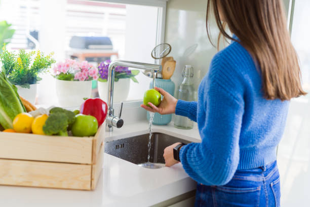 istock Young woman washing vegetables and fruit using water from sink 1214055473