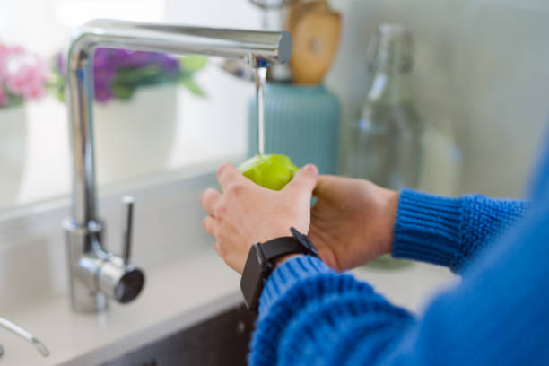 istock Young woman washing vegetables and fruit using water from sink 1214055481