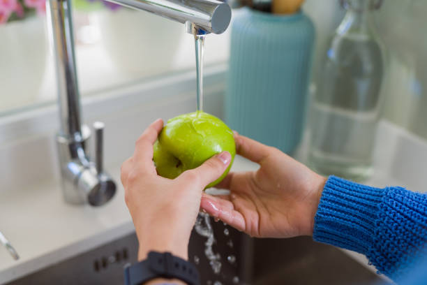 istock Young woman washing vegetables and fruit using water from sink 1214055517