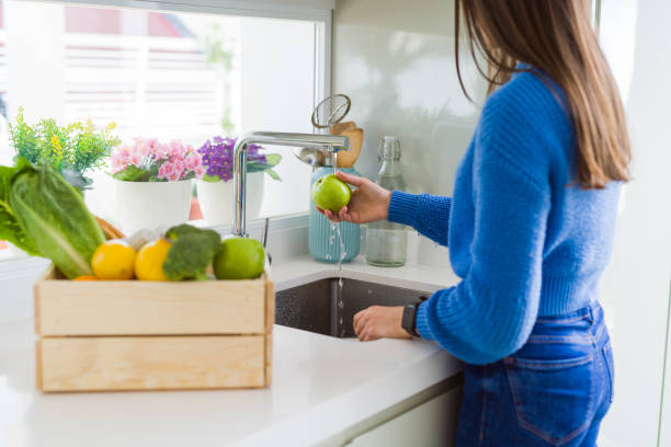 istock Young woman washing vegetables and fruit using water from sink 1214055525