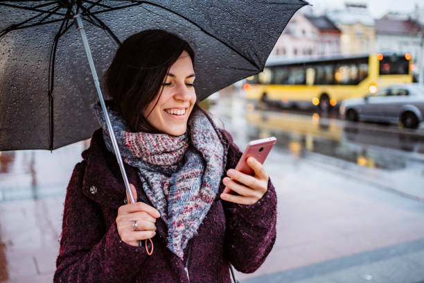 istock Woman using smartphone downtown in rain 1214057098