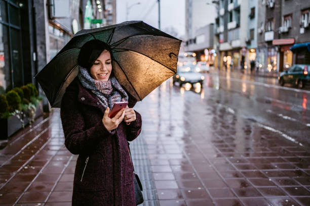 frau mit smartphone innenstadt im regen - lesen regen stock-fotos und bilder