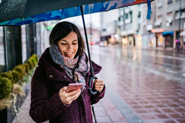 istock Woman using smartphone downtown in rain 1214057203