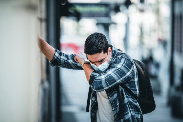 jovem usa máscara facial e tosse enquanto está na cidade. retrato de jovem com máscara facial médica está na rua da cidade. cara usando máscara protetora de vírus ao ar livre nas pessoas lotadas. conceito de vida em saúde e segurança a partir de c - smog city pollution town - fotografias e filmes do acervo