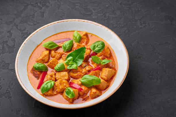 istock Thai Panang Chicken Curry in white plate at black slate background. Phanaeng Curry is thai cuisine dish with chicken, kaffir lime leaves, red curry sauce and vegetables. Thai food. Thailand meal 1214058965