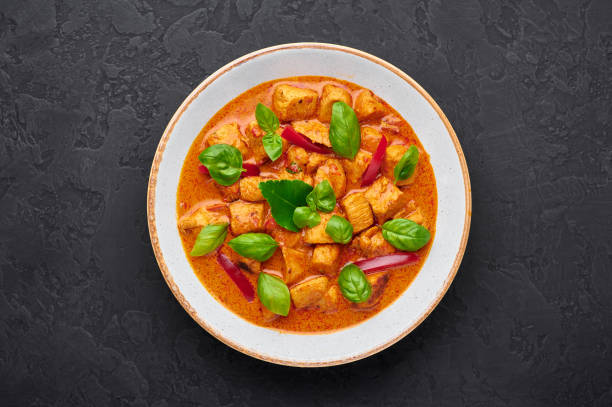 curry de poulet de panang thaïlandais dans l’assiette blanche au fond noir d’ardoise. phanaeng curry est un plat de cuisine thaïlandaise avec du poulet, des feuilles de lime kaffir, de la sauce au curry rouge et des légumes. nourriture thaïlandaise - panang curry photos et images de collection