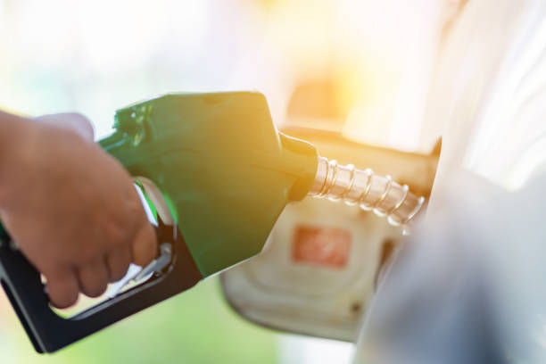 Man Handle pumping gasoline fuel nozzle to refuel. Vehicle fueling facility at petrol station. White car at gas station being filled with fuel. Transportation and ownership concept. stock photo