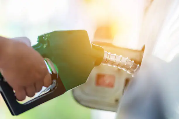 Man Handle pumping gasoline fuel nozzle to refuel. Vehicle fueling facility at petrol station. White car at gas station being filled with fuel. Transportation and ownership concept.