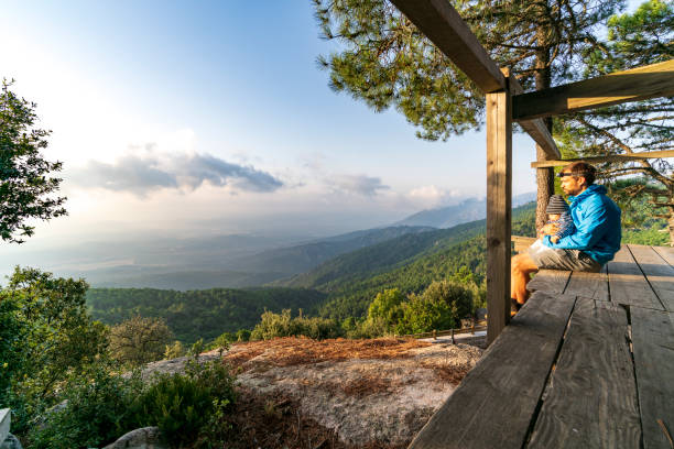 Father and son in hiking outdoor clothing watching morning landscape view from wooden platform over mountain valley landscape and mountain range, close to Ospedale, Corsica, France