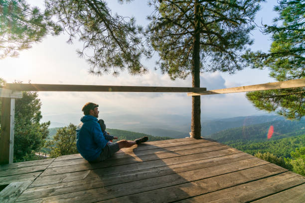 Father and son in hiking outdoor clothing watching morning landscape view from wooden platform over mountain valley landscape and mountain range, close to Ospedale, Corsica, France