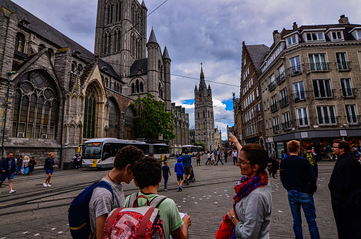Ghent, Belgium, August 2019. Two boys with their mother consult the tourist map, behind them are the church of St. Nicholas and the bell tower, the Beffroi.
