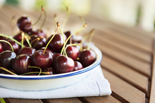 Plate full of cherries on wooden table.