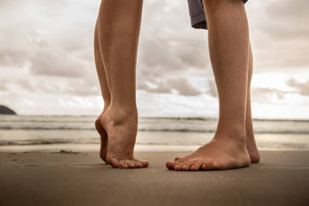 Low section of lovers at beach Low section of lovers at beach tall stock pictures, royalty-free photos & images