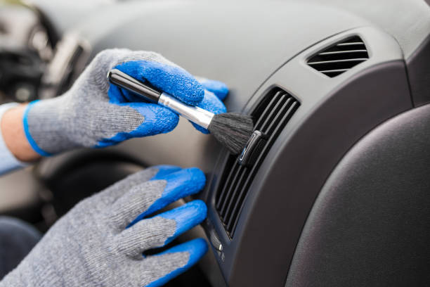 istock Professional car cleaning service. Man hands in protective gloves removing dust from air duct with soft brush. 1214083049