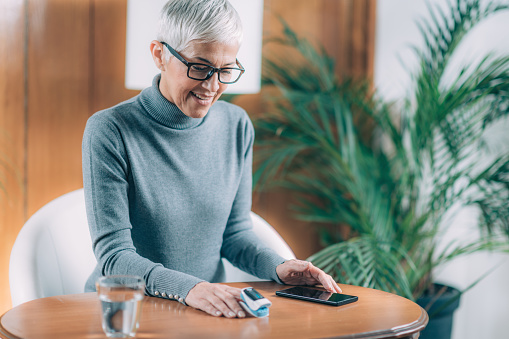 Senior Woman Using Pulse Oximeter and Smart Phone, Measuring Oxygen Saturation