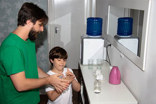 father teaching son at home to clean his hands with alcohol gel