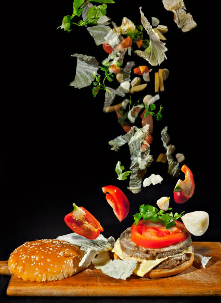 istock Vegetables isolated on black background. Pieces of meat, tomatoes, cabbage, garlic, carrots and herbs fall on a burger. Blurred as an artistic effect. Concept of motion, dynamics and flight. 1214090608
