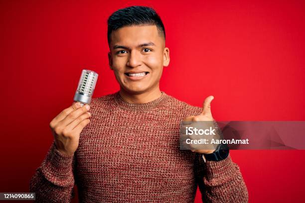 Young Handsome Latin Man Holding Led Lightbulb Over Isolated Red Background Happy With Big Smile Doing Ok Sign Thumb Up With Fingers Excellent Sign Stock Photo - Download Image Now