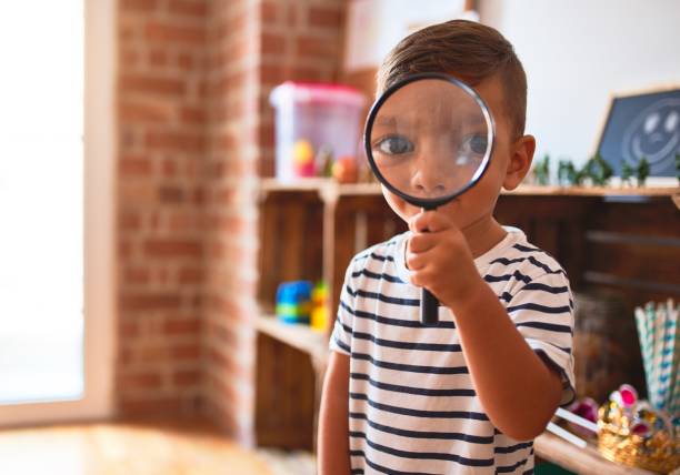 istock Beautiful toddler boy using magnifying glass at kindergarten 1214091048