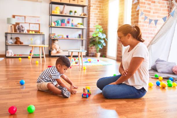 istock Beautiful teacher and toddler boy playing with train at kindergarten 1214093045