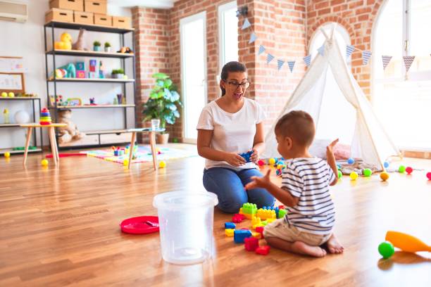istock Beautiful teacher and toddler boy playing with construction blocks bulding tower at kindergarten 1214093159