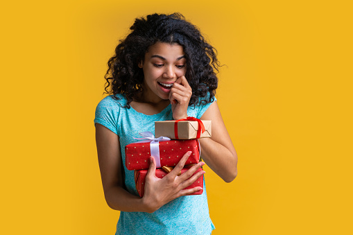 Portrait of happy young african american girl holding a bunch of gift boxes decorated with satin ribbon in hands with astonished face expresson surprised by unexpected presents.